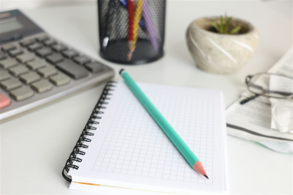 Calculadora, caderno e óculos sobre uma mesa de escritório, representando a rotina fiscal de um pequeno negócio